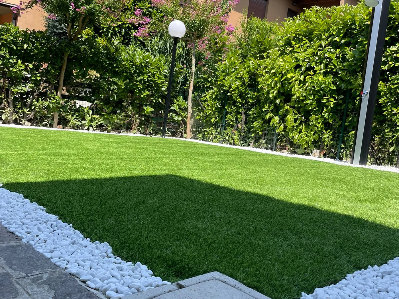 Prato sintetico realmente posato in un giardino con bordura di ciottoli bianchi